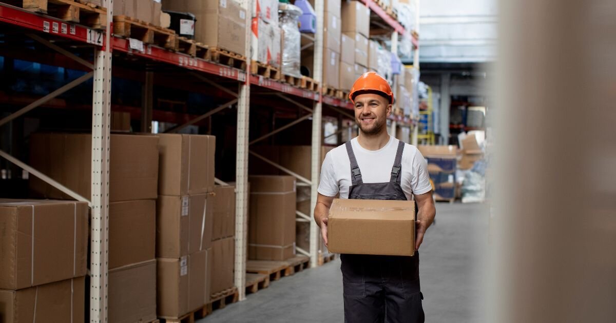 smiling man walking with a box through warehouse 